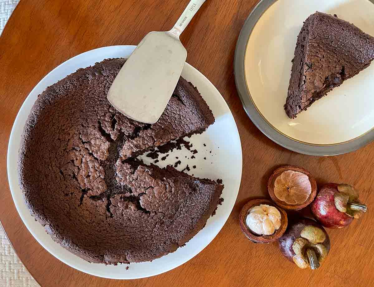 A round chocolate polenta pudding cake on a white plate with one slice cut from it on a plate nearby.