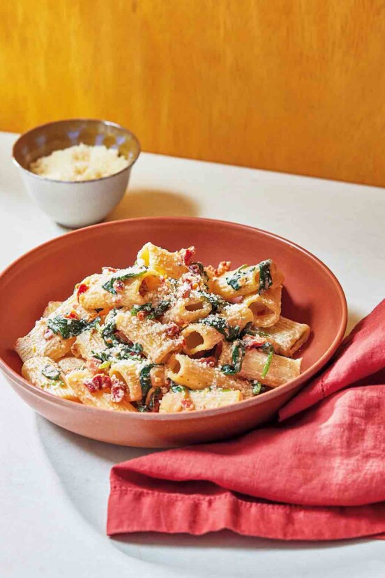 A red bowl filled with creamy sun-dried tomato and spinach pasta with a red cloth napkin on the side.