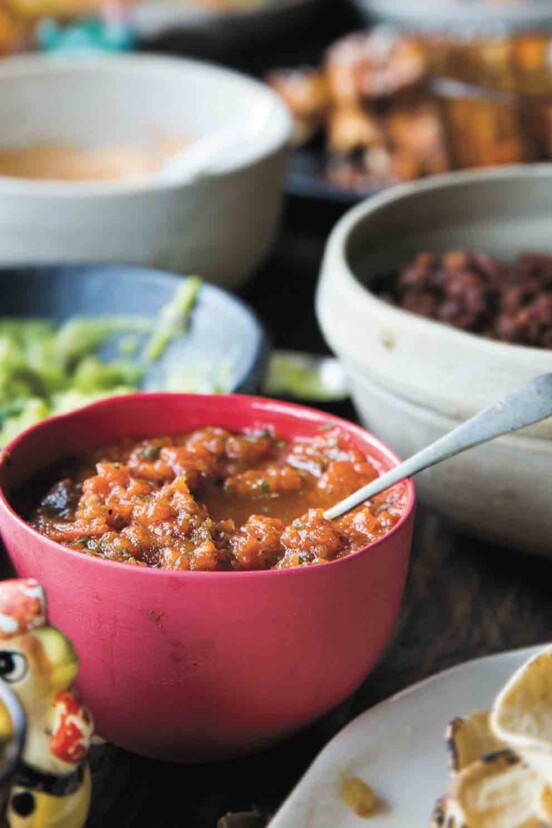 A red bowl filled with fire-roasted salsa in the middle of a Mexican feast.