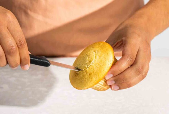 A person cutting a piece out of a vanilla cupcake.