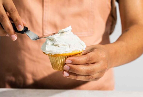 A person using an offset spatula to frost a cupcake.