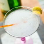 A frozen gin fizz in a martini glass with an orange stir stick and a little piece of lemon on the rim.