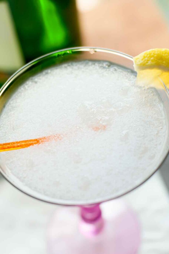 A frozen gin fizz in a martini glass with an orange stir stick and a little piece of lemon on the rim.