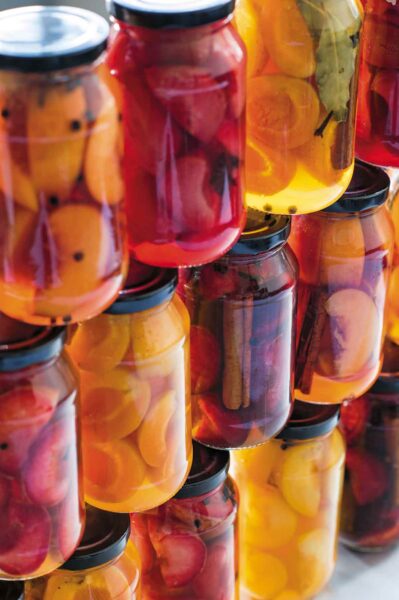 An assortment of pickled stone fruits in jars stacked on top of each other.