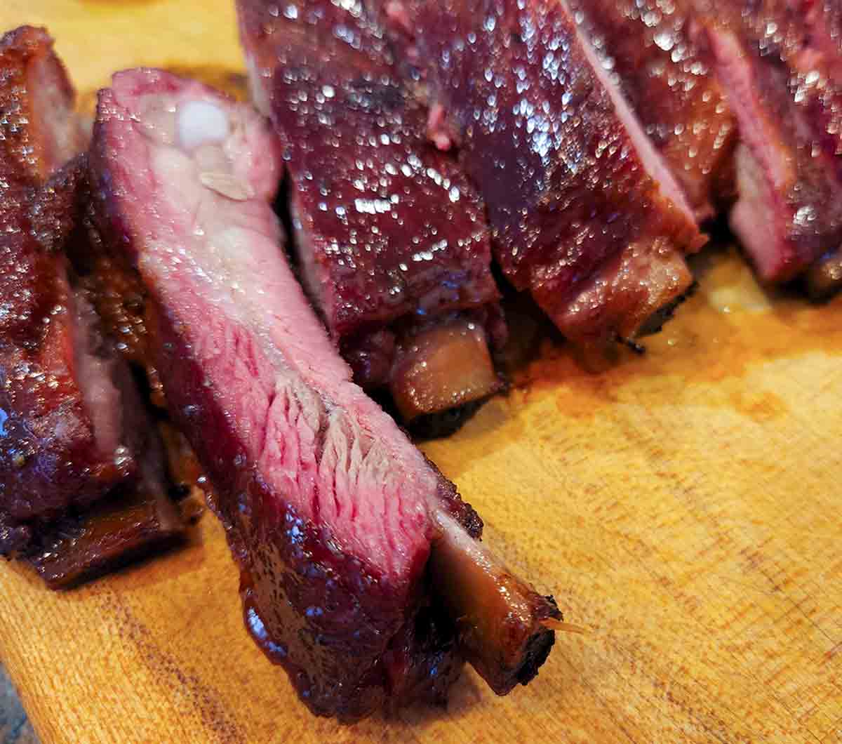 A rack of smoked pork ribs cut into individual ribs on a wooden cutting board.