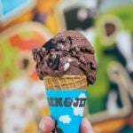 A hand holding a scoop of Ben & Jerry New York super fudge chunk in a sugar cone.