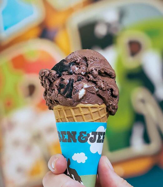 A hand holding a scoop of Ben & Jerry New York super fudge chunk in a sugar cone.