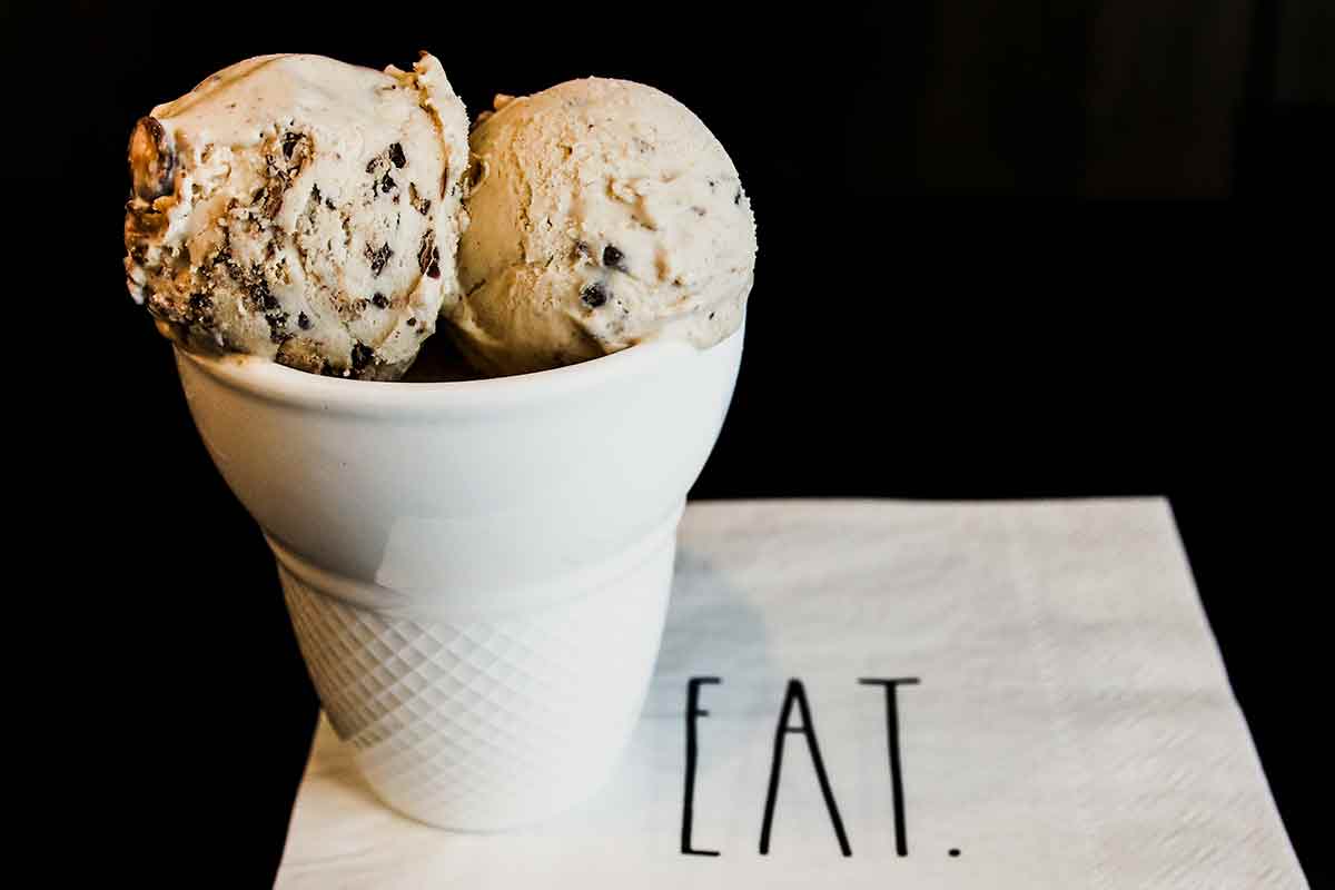 Two scoops of no-churn peanut butter cup ice cream in a bowl shaped like a cone, on a napkin with the word 'eat' on it.