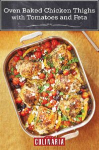 A metal roasting pan filled with roasted chicken thighs, olives, lemon, tomatoes, feta, and herbs.