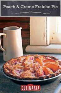 A peach and crème fraîche pie sitting on a window sill with a pitcher nearby.