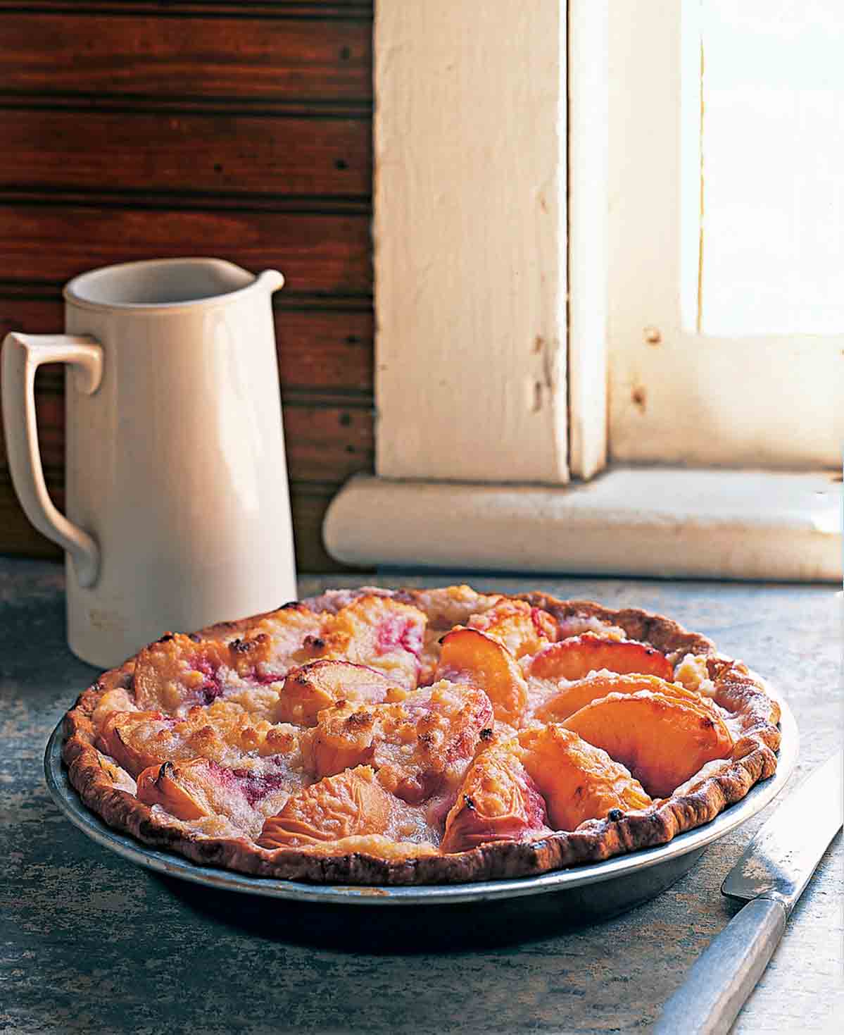 En persika- och crème fraîchepaj som sitter på en fönsterbräda med en kanna i närheten.