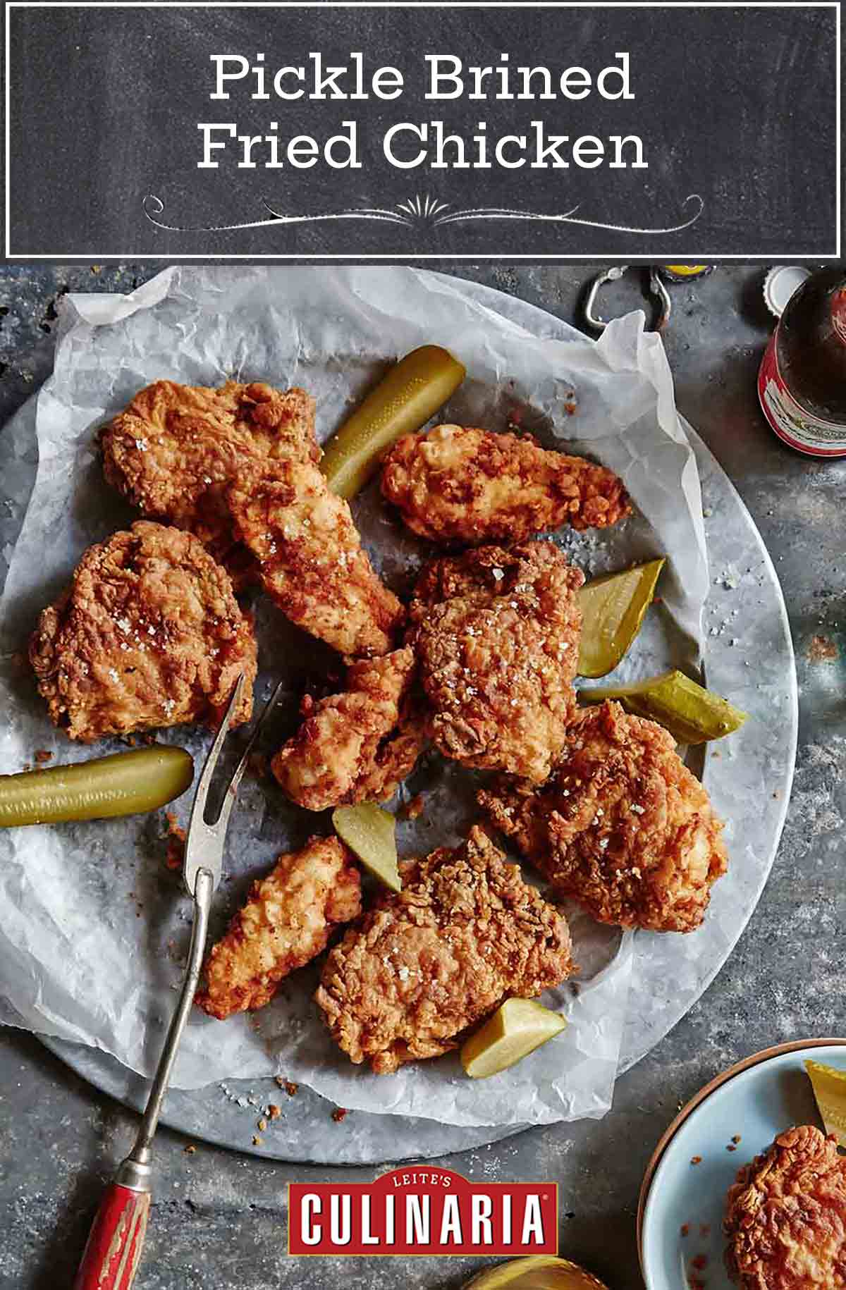 A platter of pickle-brined fried chicken with pieces of dill pickle, and a bottle of beer.