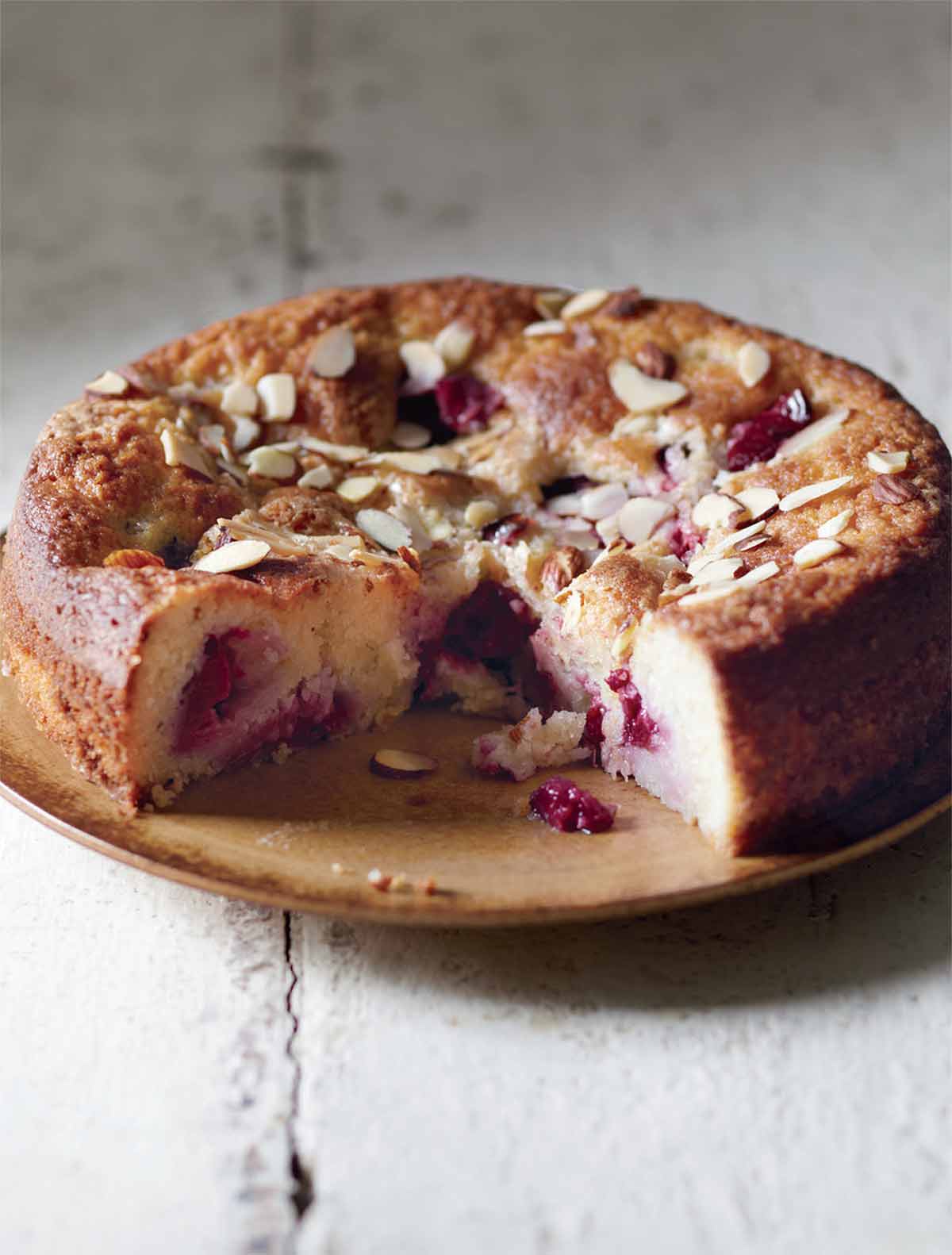 A whole plum almond cake on a plate with one wedge cut from it.