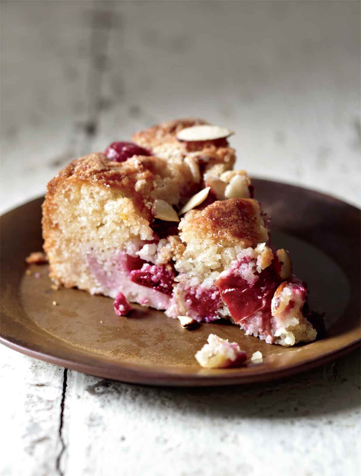 A slice of plum almond cake on a brown ceramic plate.