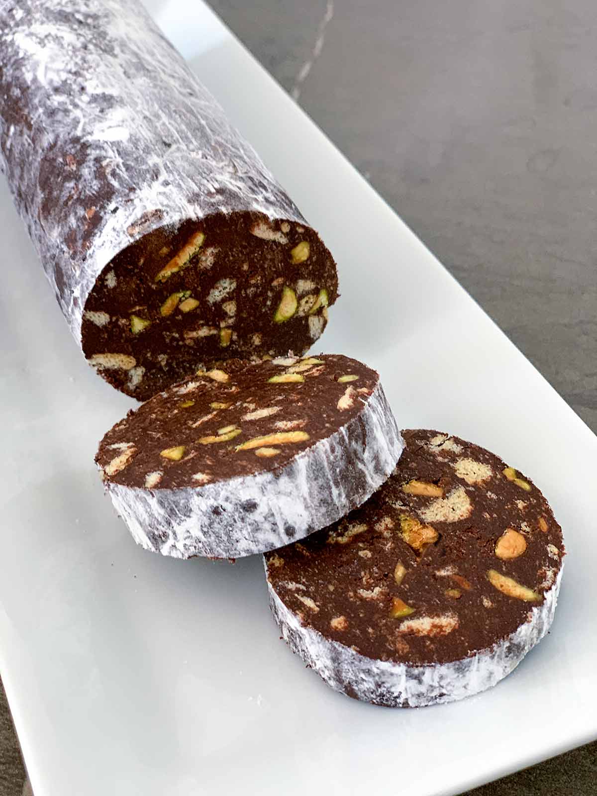 A log of chocolate salami with two slices cut from the end on a white rectangular platter.