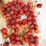Roasted cherry tomatoes on the vine on a sheet of parchment paper.