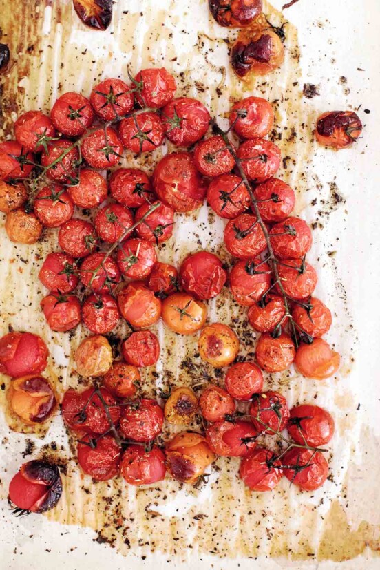 Roasted cherry tomatoes on the vine on a sheet of parchment paper.