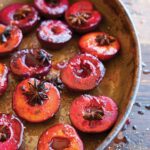 An oval dish filled with roasted plums, topped with star anise.