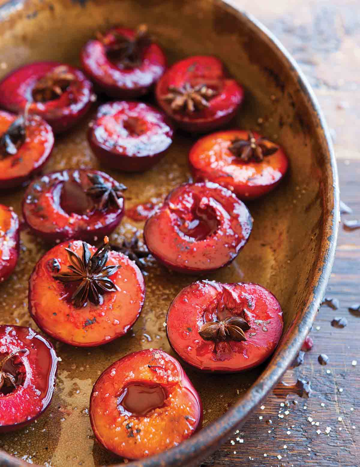 An oval dish filled with roasted plums, topped with star anise.