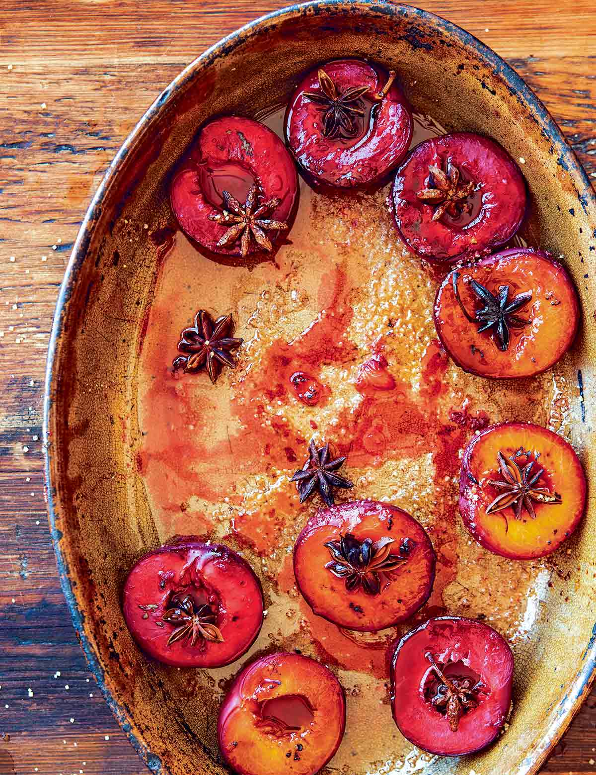 An oval dish filled with roasted plums, topped with star anise.