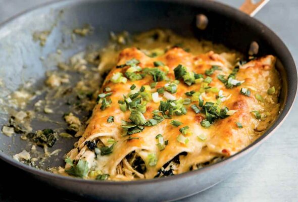 Four chicken enchiladas in a nonstick skillet, topped with scallions.
