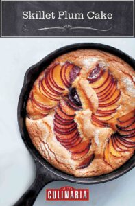 A cast-iron skillet plum cake with slices of fanned out plums baked in.