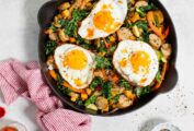 A cast-iron skillet filled with sweet potato and chicken sausage hash, topped with three fried eggs.