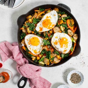 A cast-iron skillet filled with sweet potato and chicken sausage hash, topped with three fried eggs.