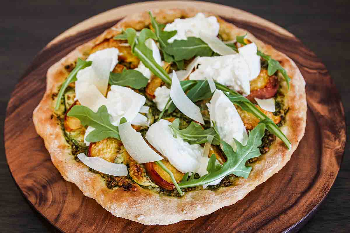 An individual-sized zucchini, peach, and burrata pizza on a round wooden platter.