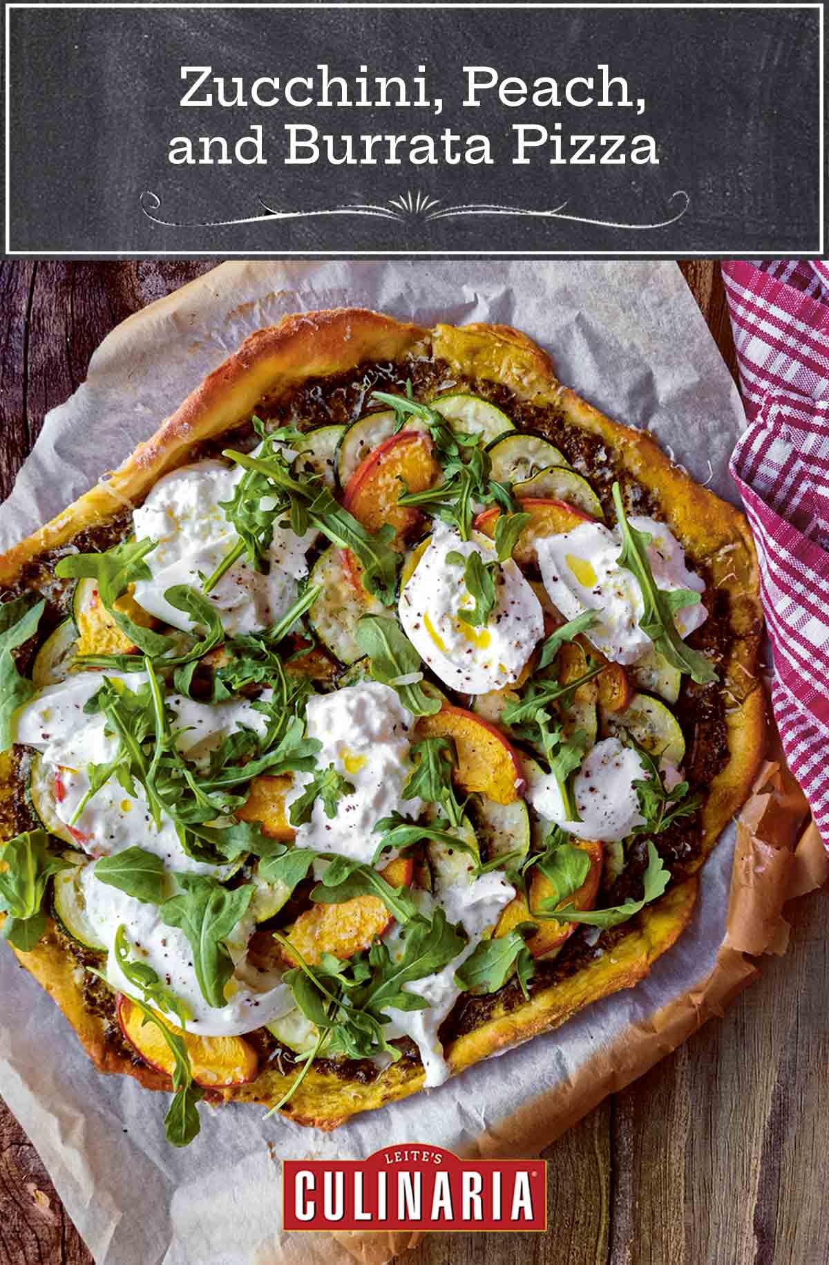 A whole zucchini, peach, and burrata pizza, topped with arugula, on a piece of parchment on a wooden surface.