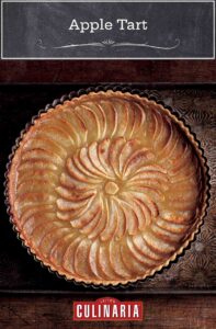 A round tart filled with cooked sliced apples in a concentric pattern.