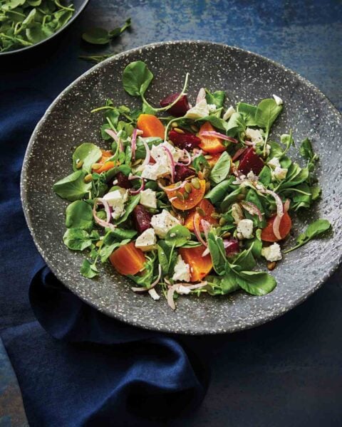 Gray speckled bowl of beet salad with feta and pumpkin seeds, along with spinach and sliced red onions.