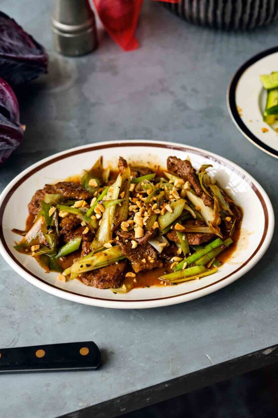 A white and brown plate filled with beef and leek stir fry, topped with peanuts.