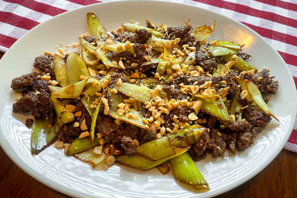 A white plate filled with beef and leek stir fry, topped with peanuts.