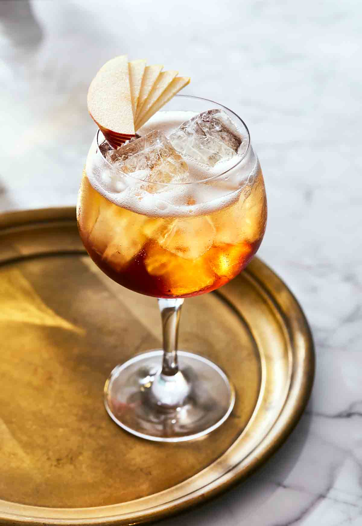 A wine glass filled with ice, amber liquid, a little foam on top, and an apple fan garnish.