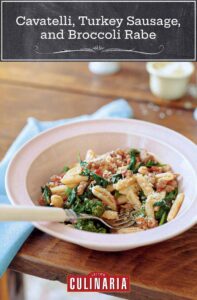 Bowl of cvatelli with turkey sausage, tomato, and broccoli rabe on a table, with a spoon.