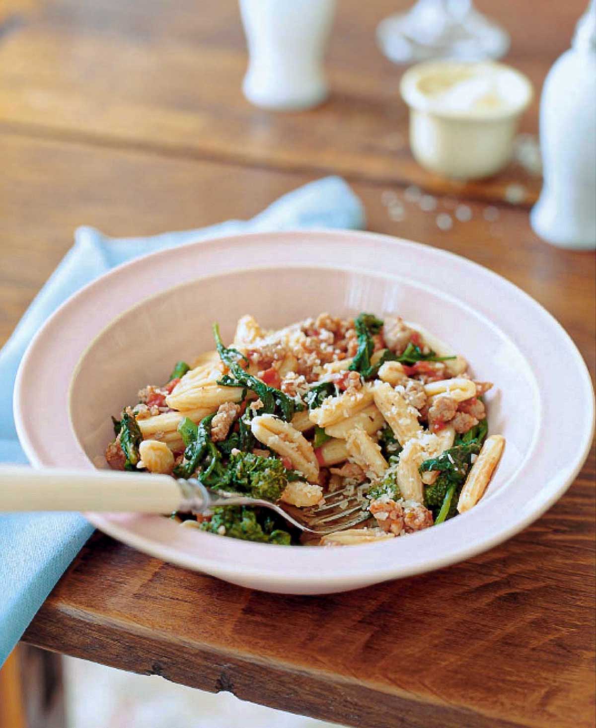Bowl of cvatelli with turkey sausage, tomato, and broccoli rabe on a table, with a spoon.