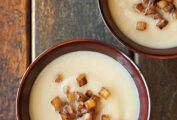 Two bowls of pureed celery root soup topped with cubes of caramelized apple.