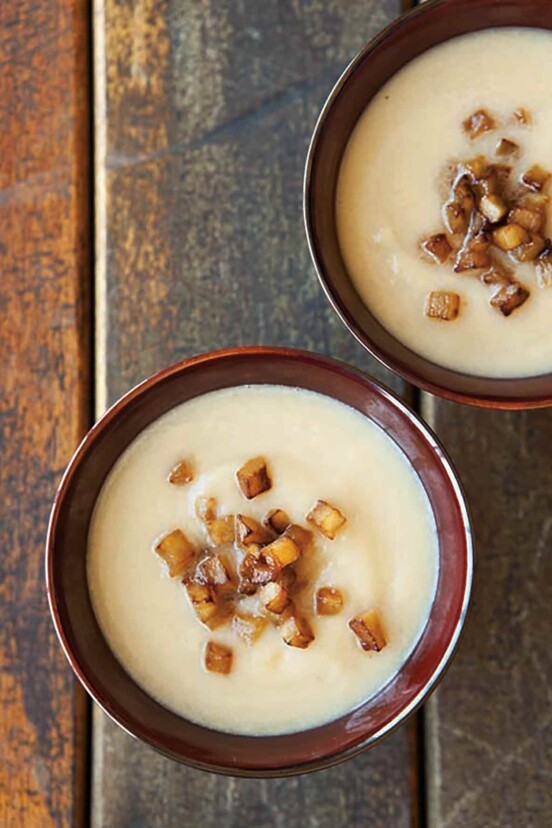 Two bowls of pureed celery root soup topped with cubes of caramelized apple.