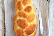 A loaf of braided challah bread on a baking sheet with a serrated knife.