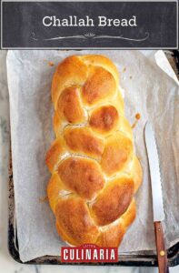A loaf of braided challah bread on a baking sheet with a serrated knife.