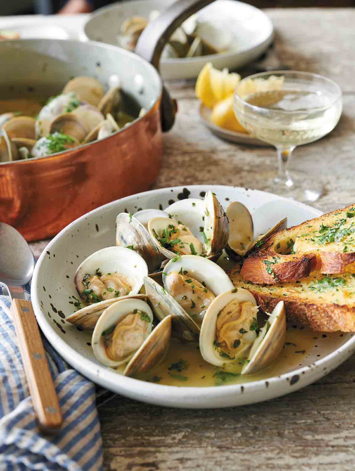 A white speckled bowl filled with opened clams with butter and parsley, and two sourdough toasts on the side of the bowl.