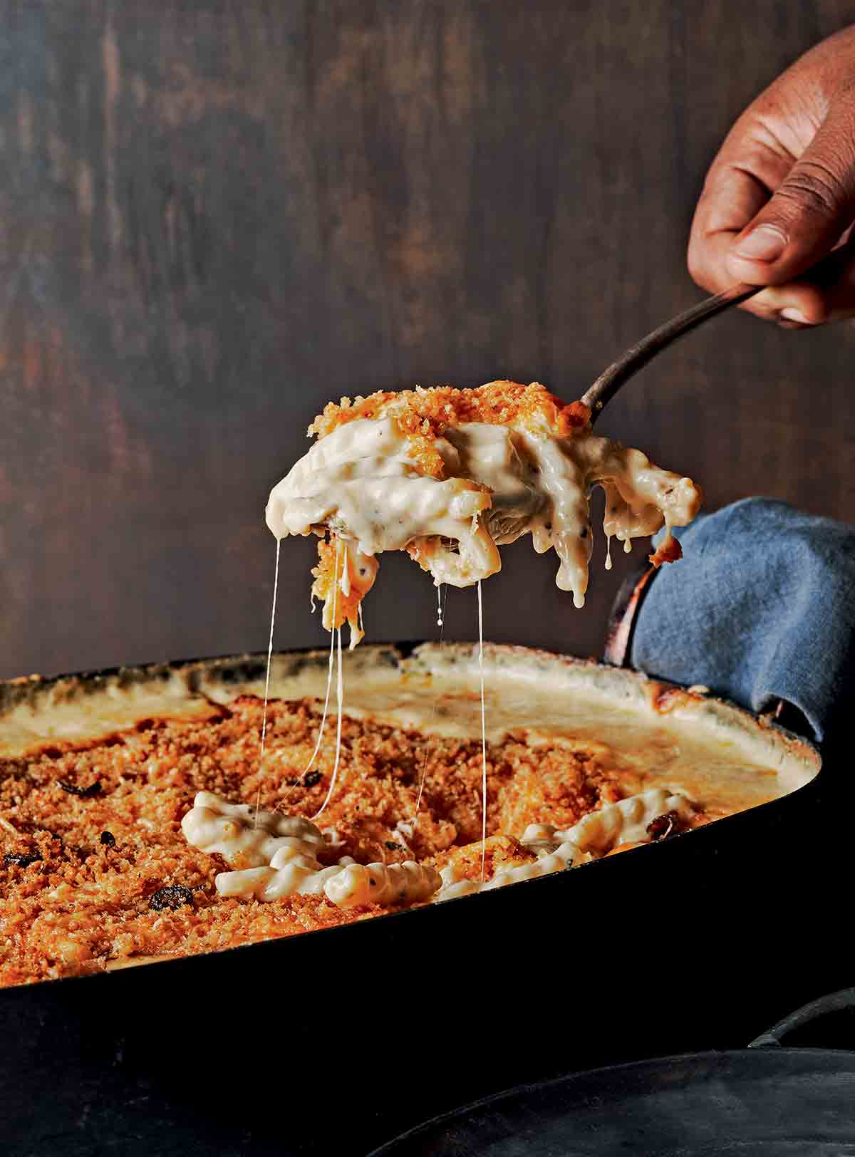 A scoop of creamy baked mac and cheese with crunchy topping being lifted from a casserole dish.