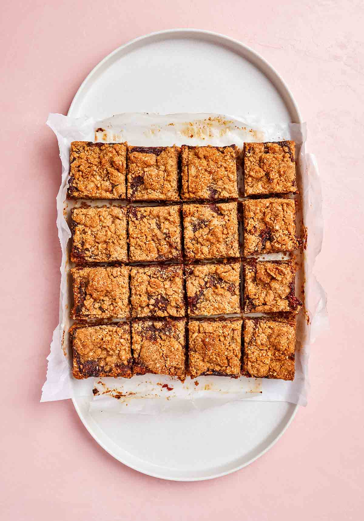 Sixteen date bars on a piece of parchment paper on a round oval tray.