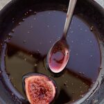 A black skillet with figs in Port wine and a spoon on the side.
