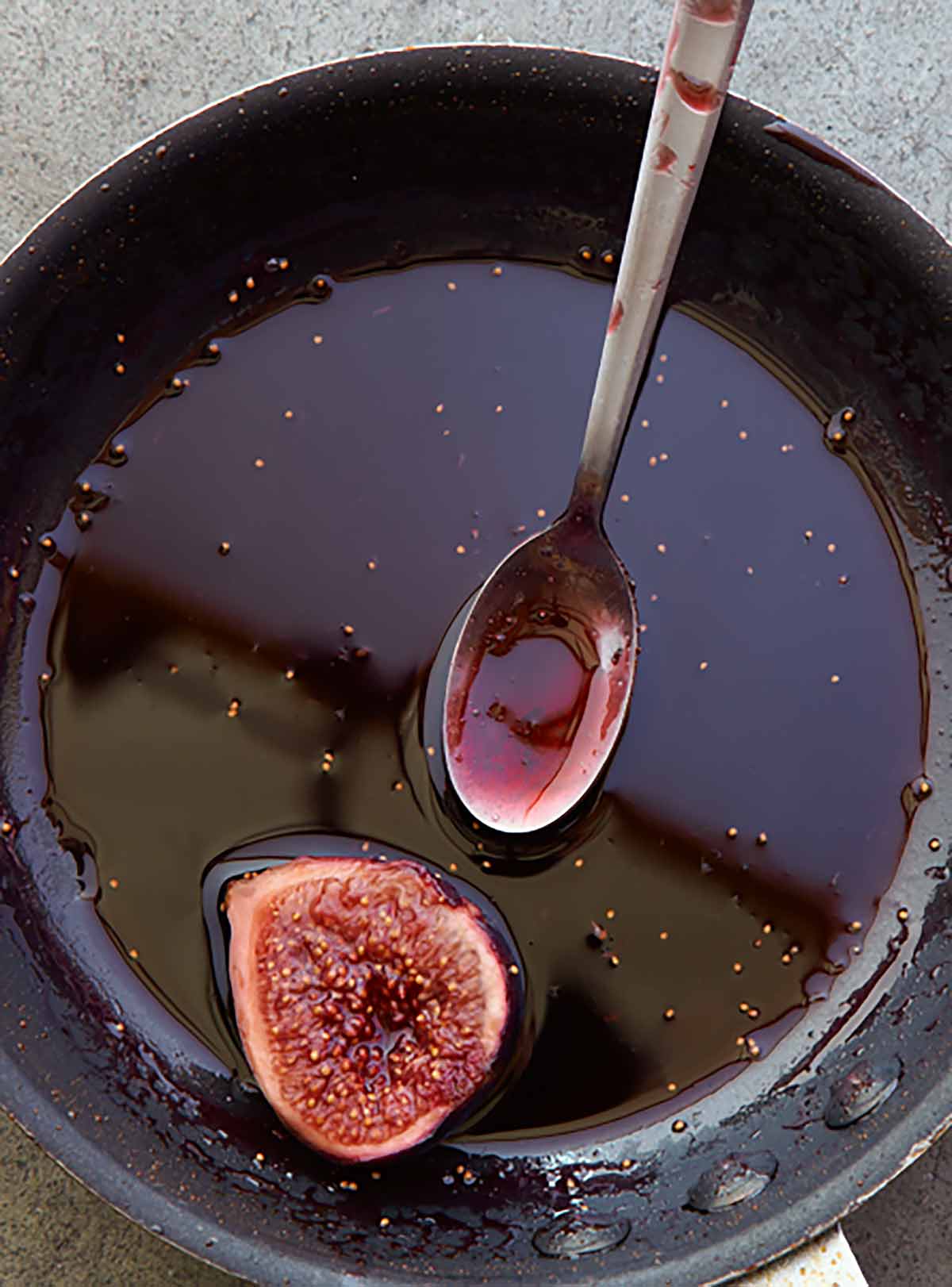 A black skillet with figs in Port wine and a spoon on the side.