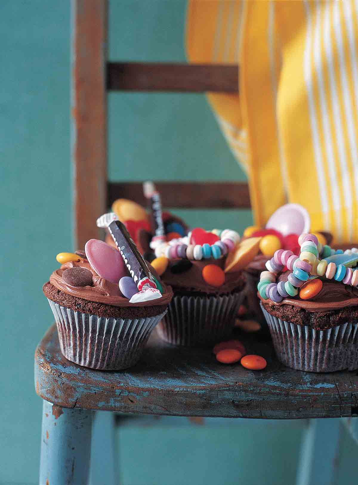 العديد من كب كيك الشوكولاتة مع صقيع الشوكولاتة والحلوى في الأعلى على كرسي خشبي.