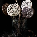 Four chocolate covered apple slices with a spider web design in a jar.