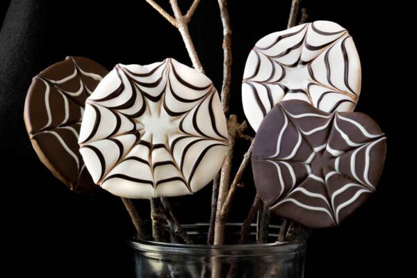 Four chocolate covered apple slices with a spider web design in a jar.