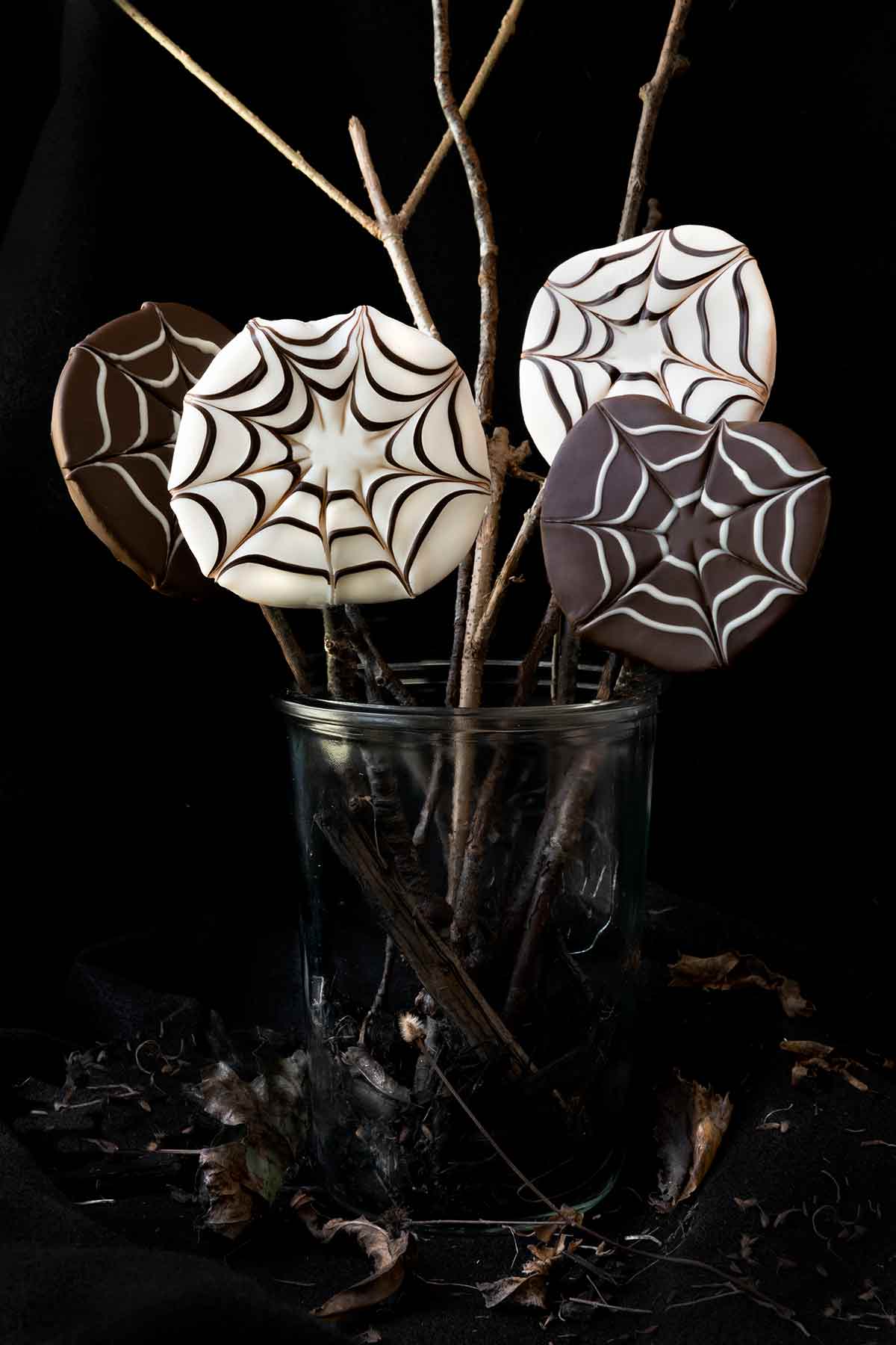 Four chocolate covered apple slices with a spider web design in a jar.